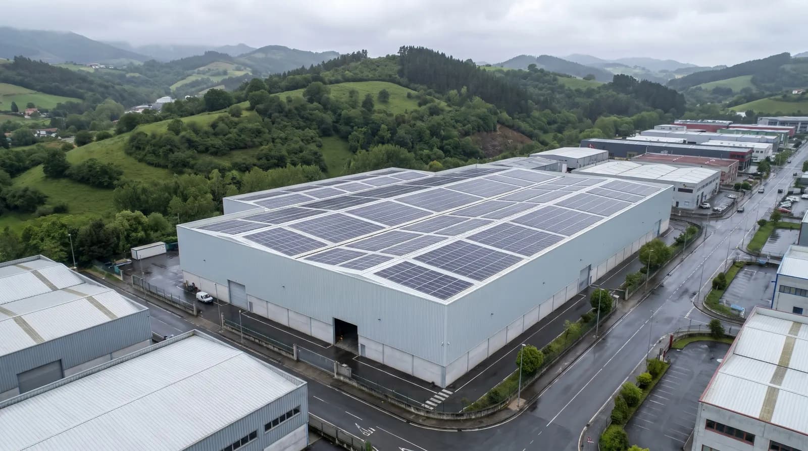 Nave industrial con la cubierta llena de placas solares en un polígono rodeado de montes verdes